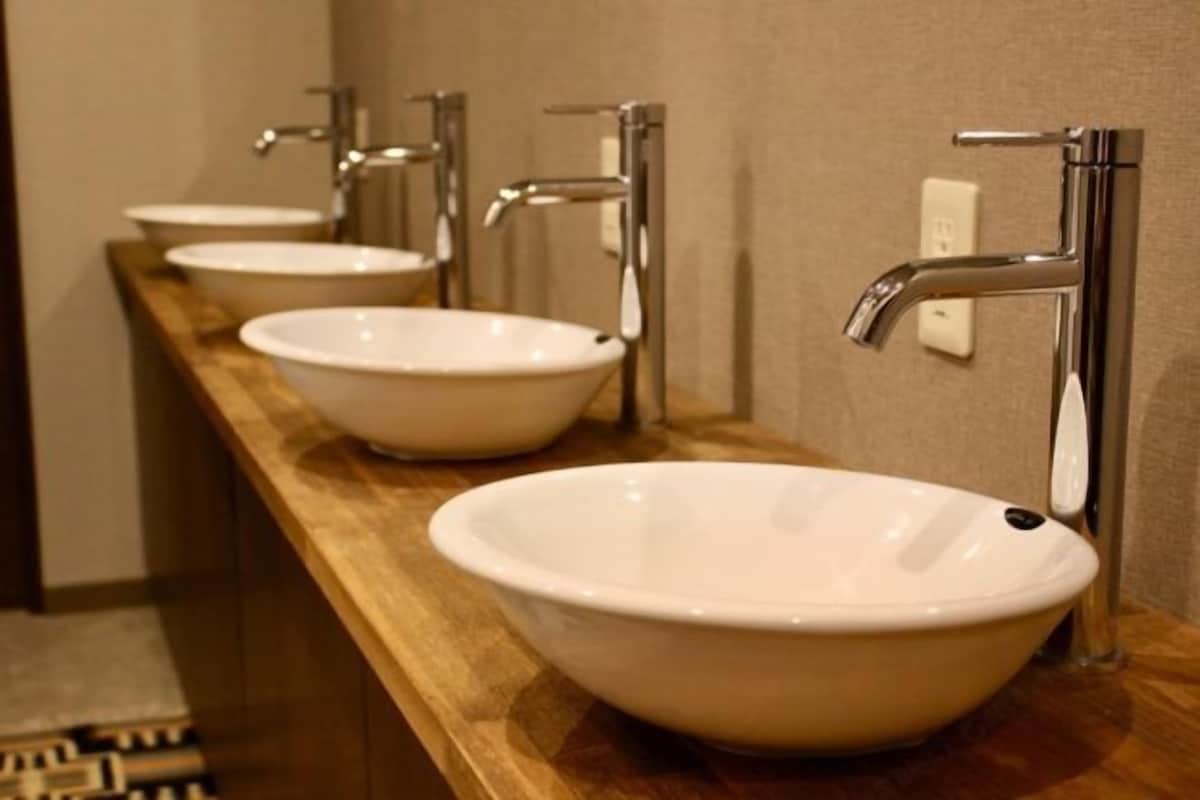 Een rij witte wasbakken met chromen kranen op een houten aanrecht in een badkamer.