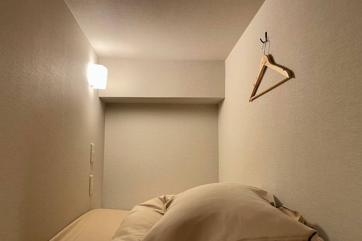 A small, dimly lit room with a bed, a hanging light fixture, and a wooden hanger on the wall.