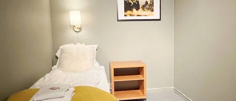A bedroom with a bed, a bedside table, a wall-mounted light, and a framed picture.