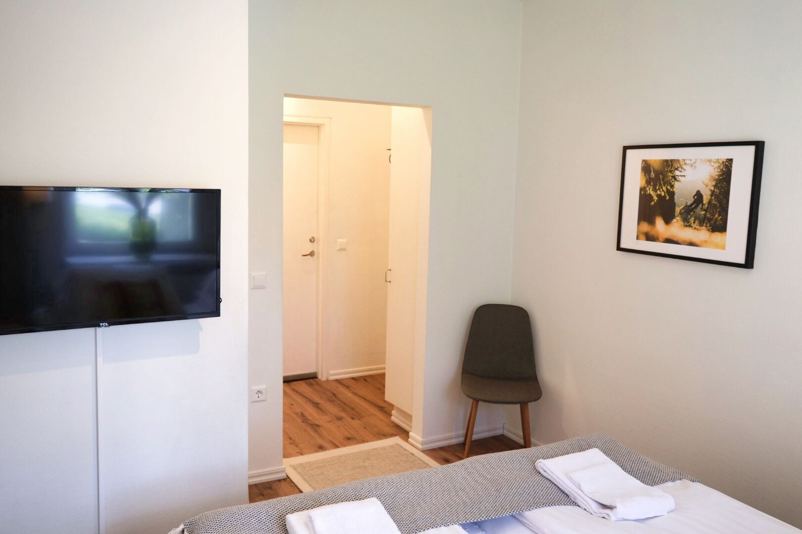 Una habitación de hotel con cama, una silla, un televisor y una puerta que da a otra habitación.