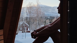 Una persona sentada en un banco de madera en una habitación con vista a un paisaje nevado y montañas.