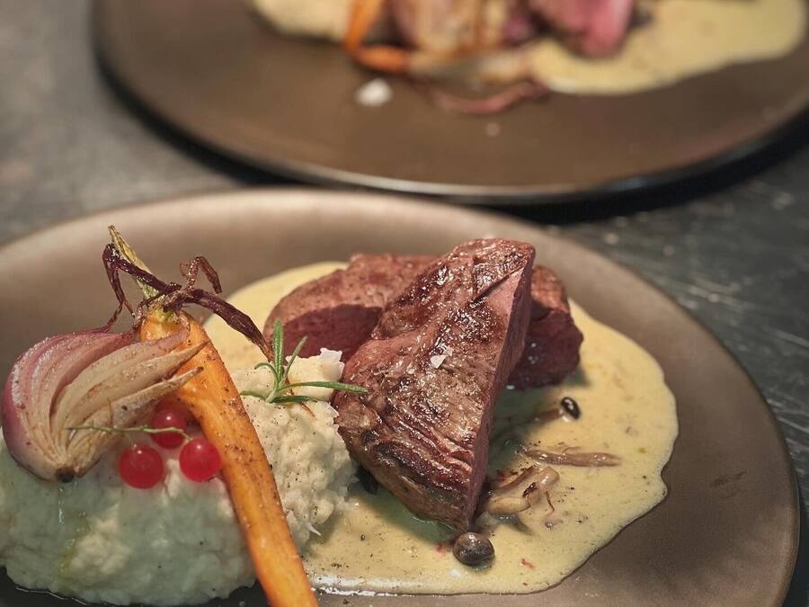 A plated dish with meat, vegetables, and a creamy sauce.