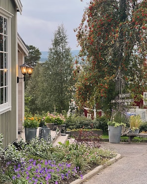 A garden with various plants and flowers, a wooden deck, and a building with a window and a lamp post. - Hotell Åre Fjällsätra (Undersaker)