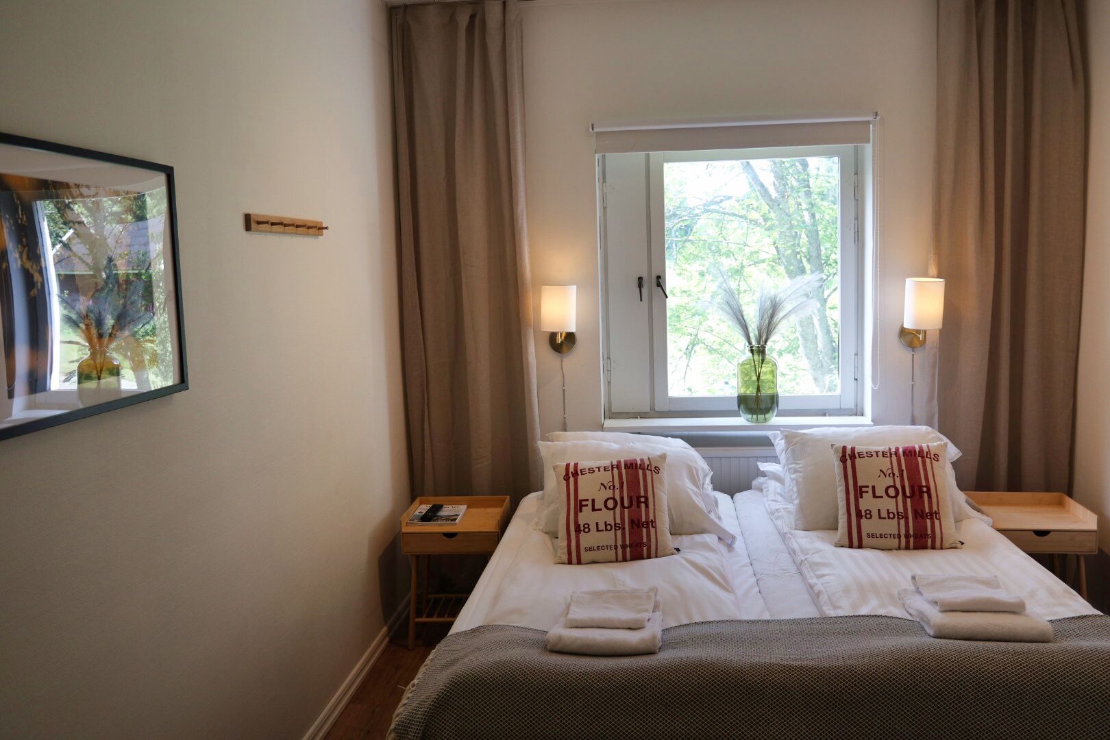 Une chambre d’hôtel avec un lit, deux tables de chevet, une fenêtre avec des rideaux et un tableau encadré au mur.