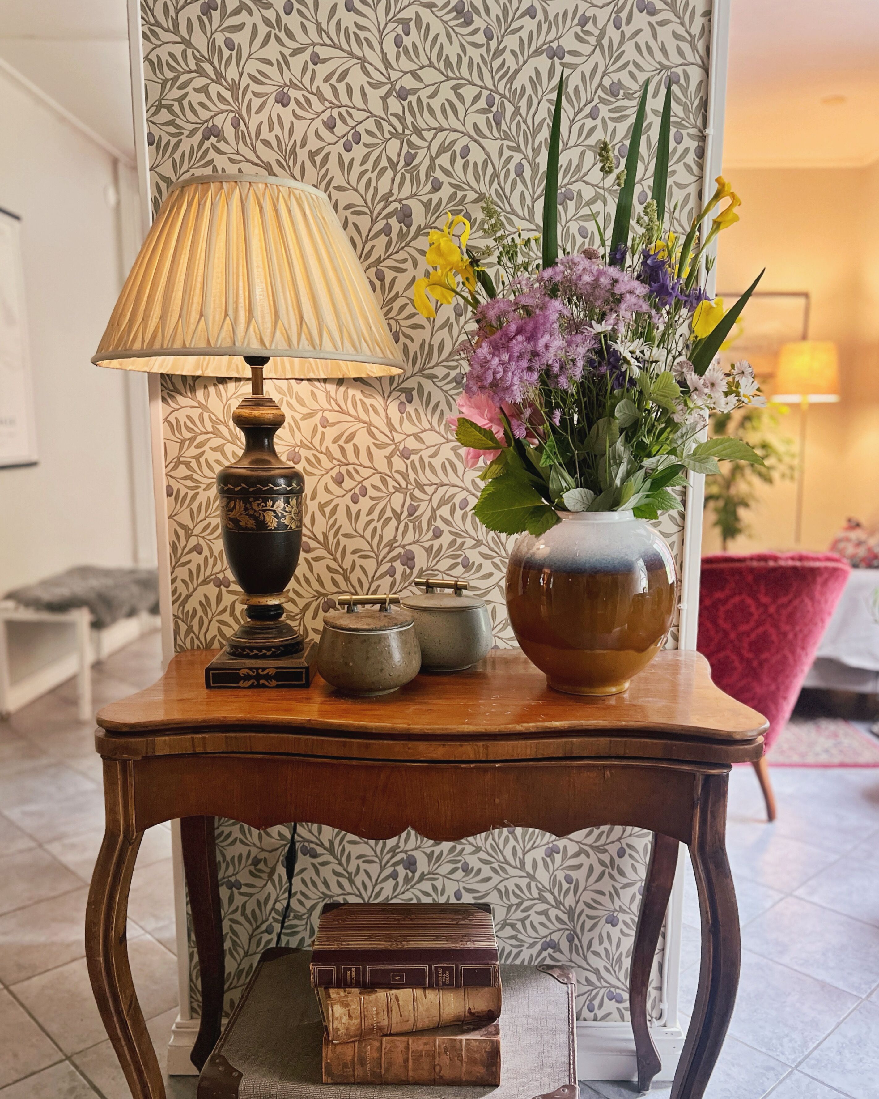 Una mesa de madera con una lámpara, un jarrón con flores y libros.