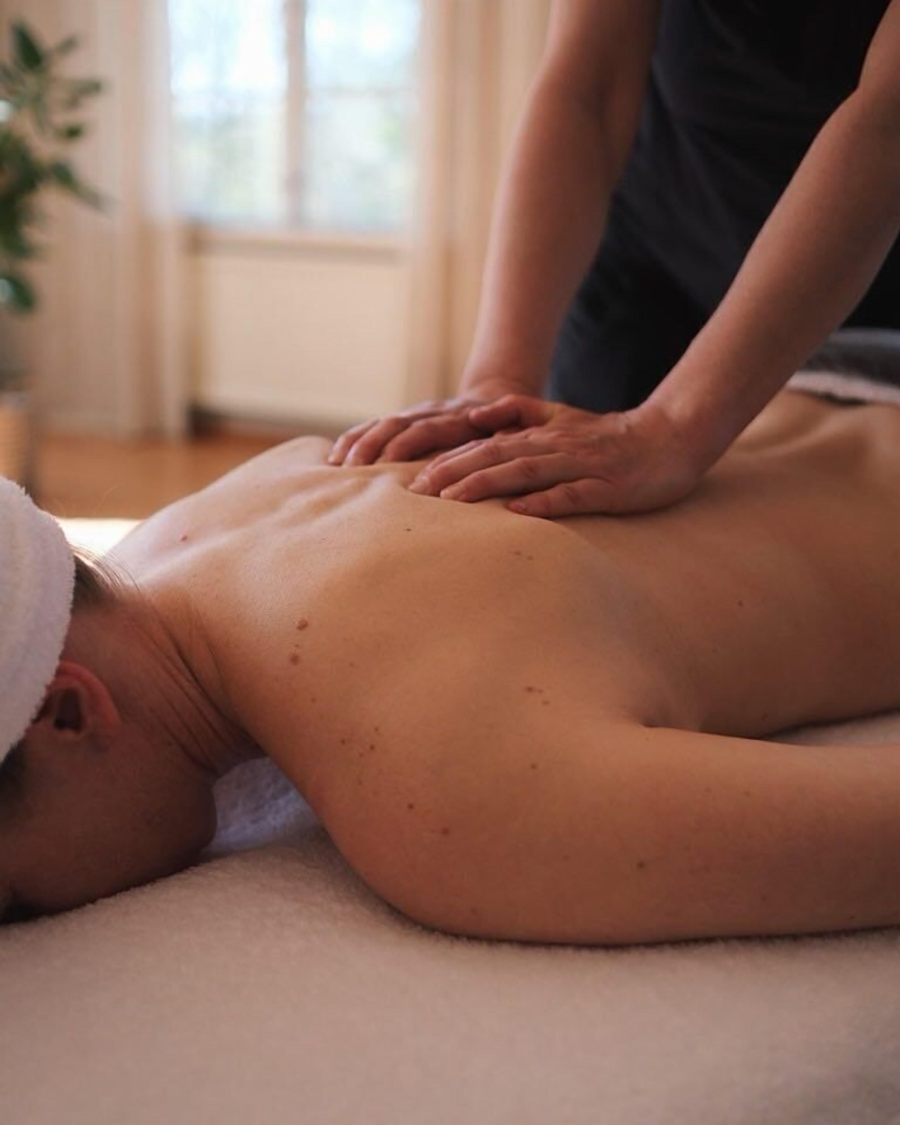 A person receiving a back massage on a massage table in a room with a window and a plant.