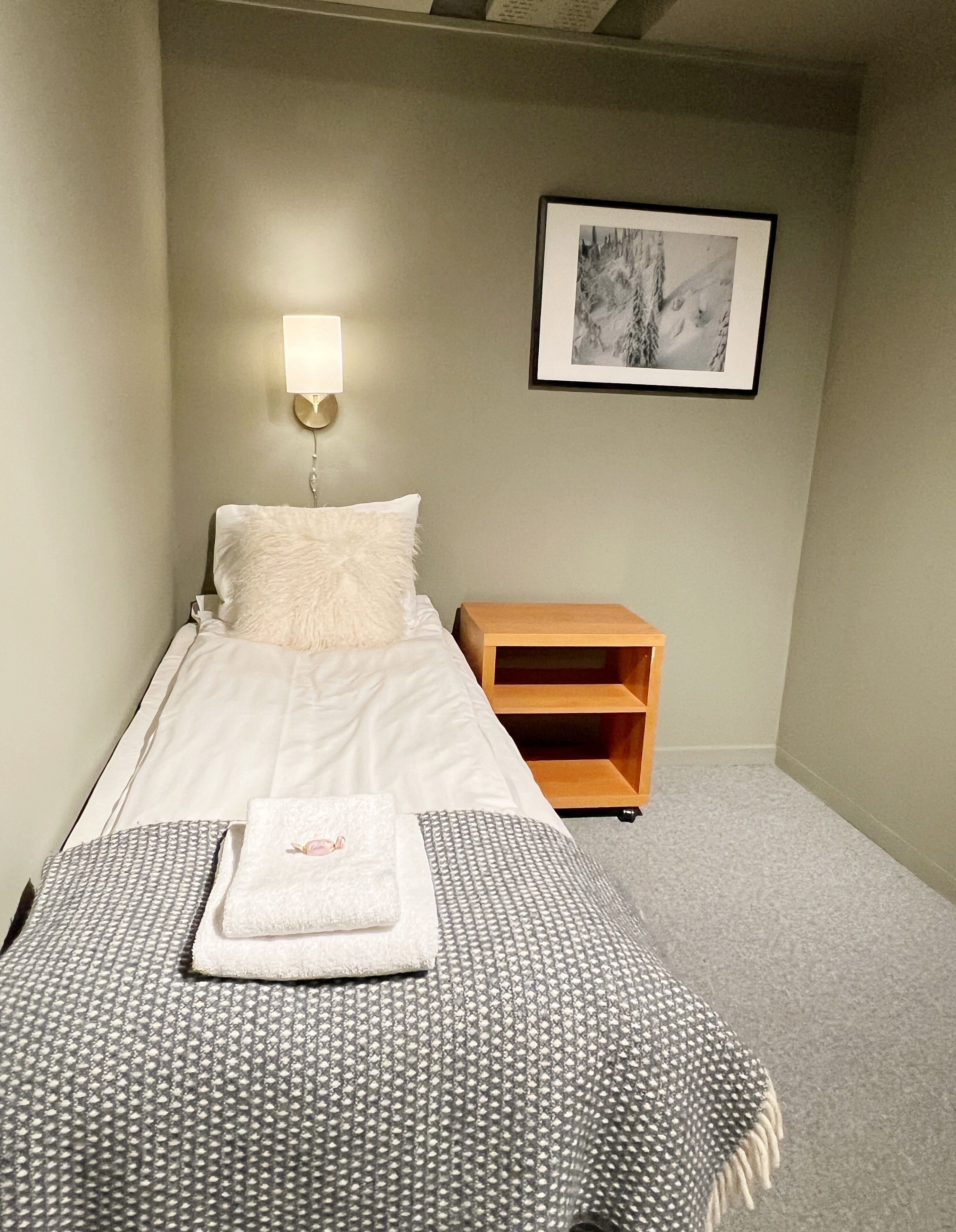 Uma cama bem arrumada com um travesseiro fofo, uma mesa de cabeceira com abajur e um quadro na parede.