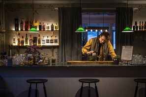 A bar area with a bartender preparing drinks, shelves with bottles, and stools. - Hotell Åre Fjällsätra (Undersaker)