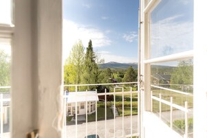 Vista desde un balcón con barandilla, sobre un paisaje verde con árboles y una casa.