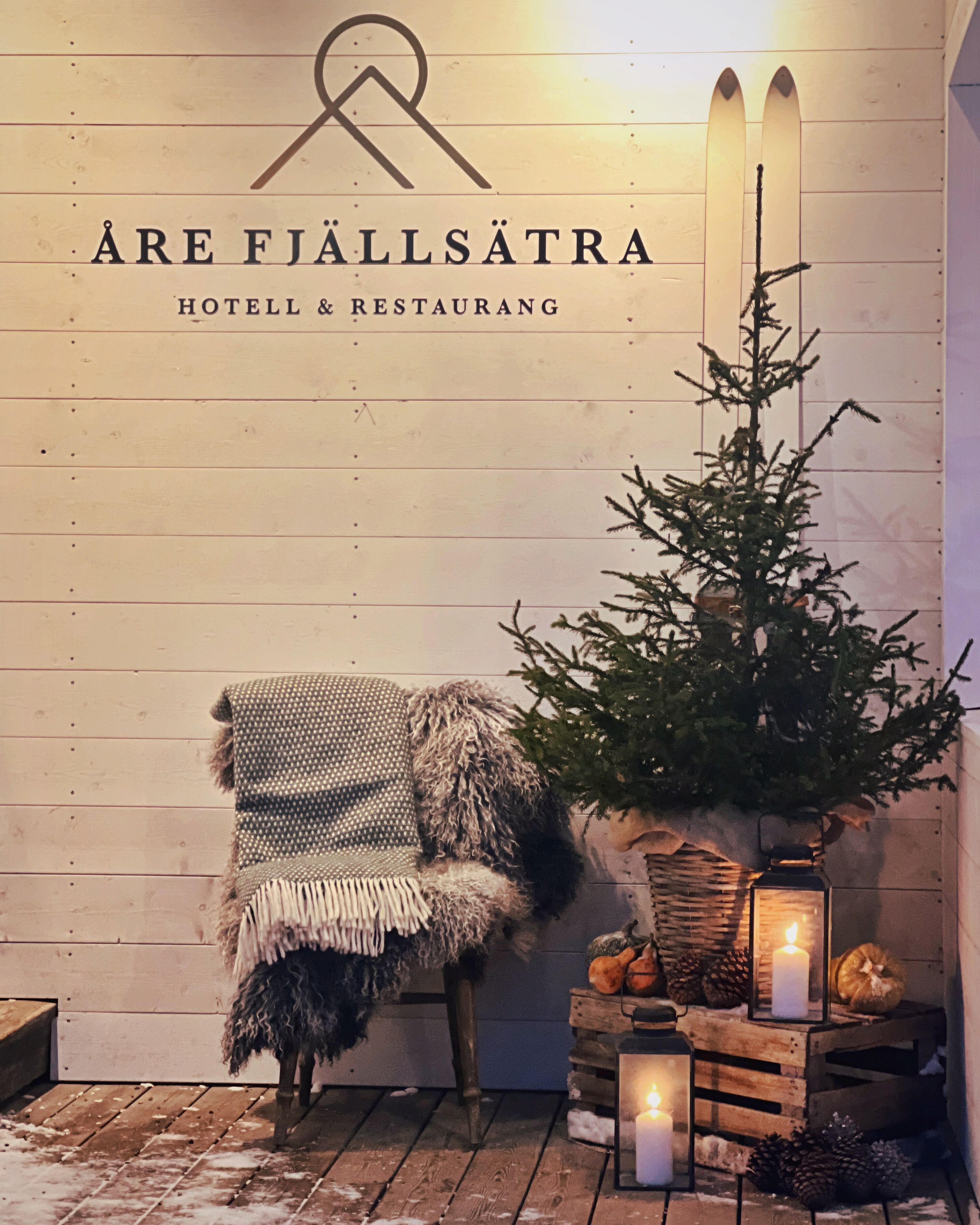 A cozy corner with a chair, a Christmas tree, and a candle on a wooden table, indicating a warm and inviting atmosphere.