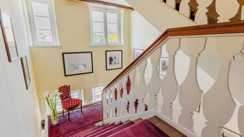 A staircase with a wooden handrail and white balusters, leading to a room with a red carpet and a chair with a red cushion.