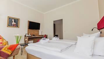 Habitación de hotel con dos camas, un televisor de pantalla plana, un escritorio de madera, una silla y un cuadro en la pared.
