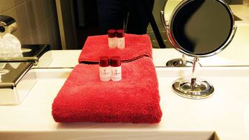 A red towel on a white counter with two bottles of body lotion and a round mirror.