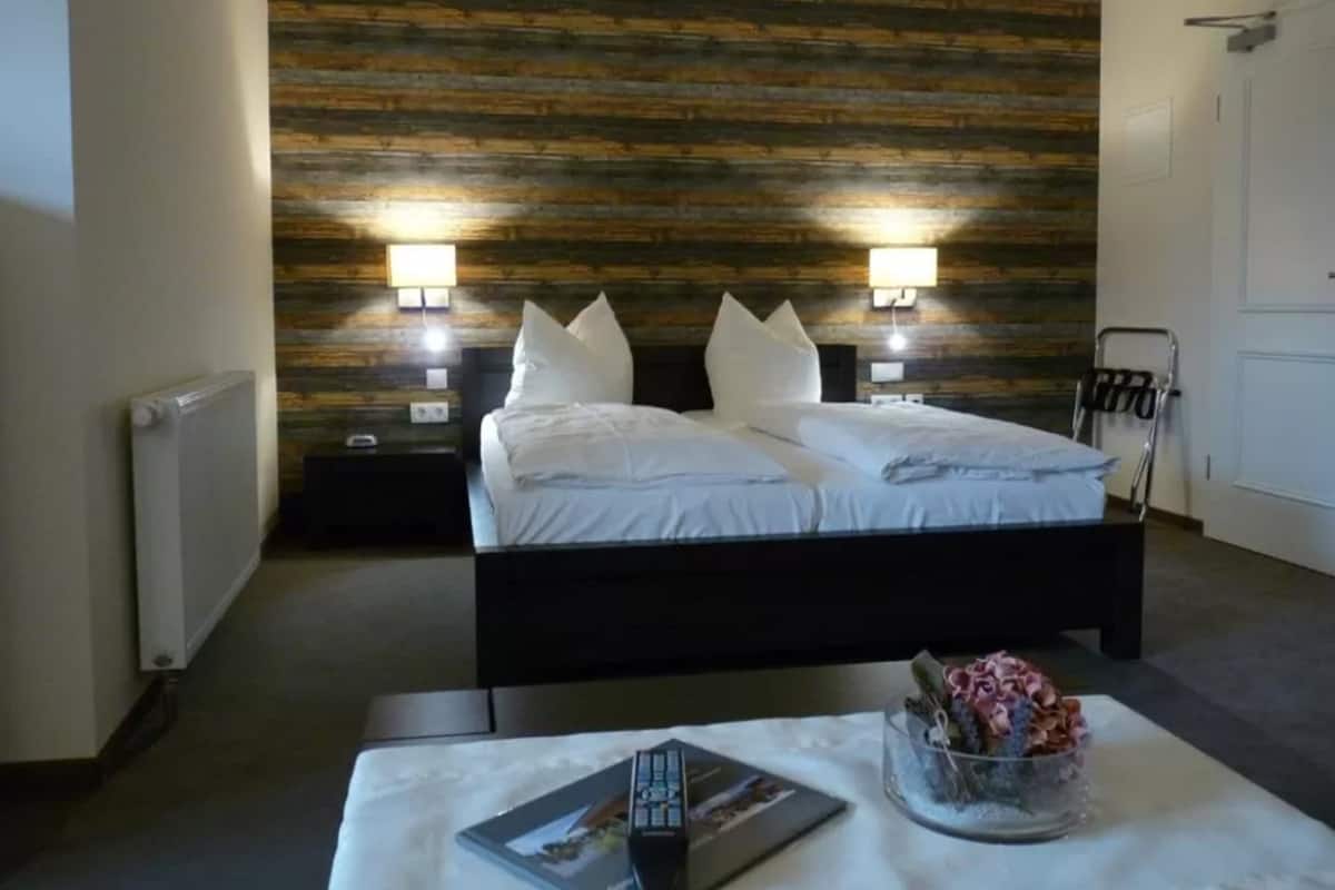 Een hotelkamer met een modern design, met een groot bed met wit beddengoed, twee bedlampen en een houten accentmuur.