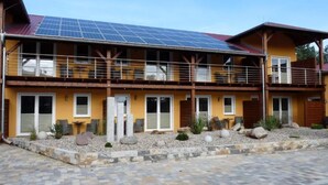 Ein zweistöckiges Gebäude mit Solaranlage auf dem Dach, einem Balkon und einem gepflasterten Eingangsbereich.