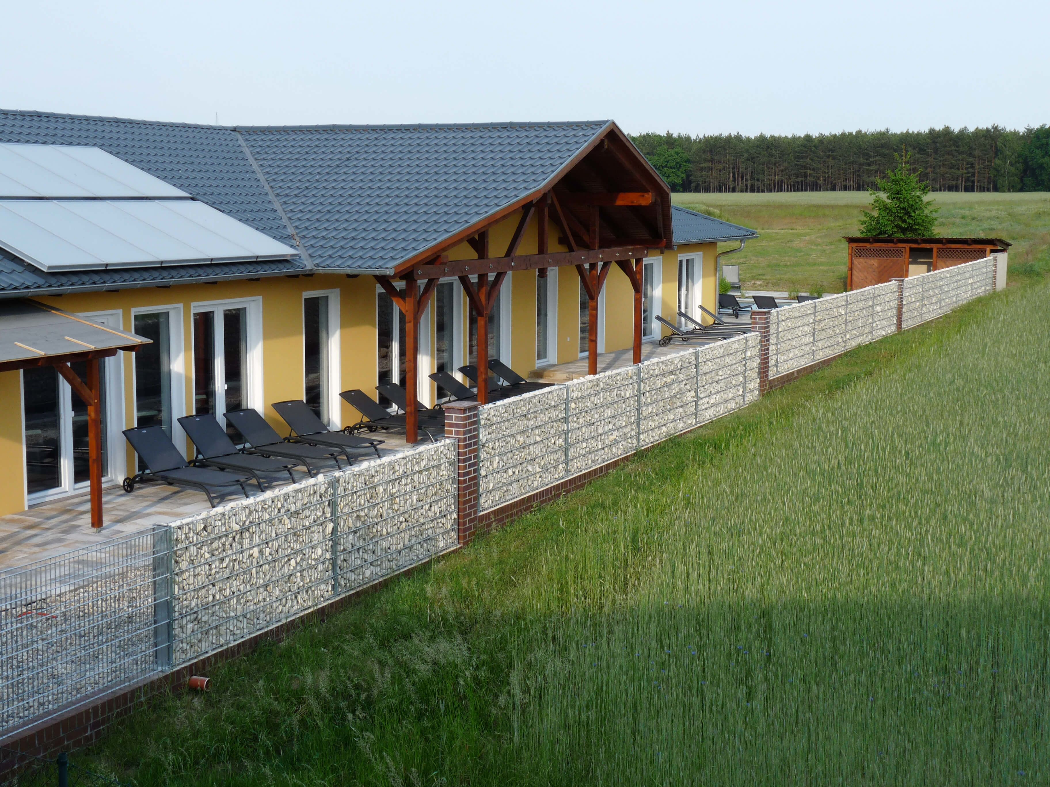 Ein Gebäude mit überdachter Terrasse, mehreren Liegestühlen und einer Steinmauer.