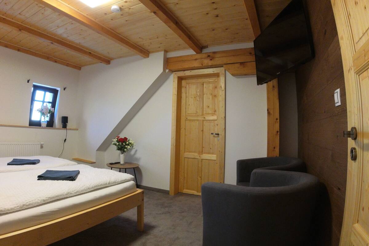 A bedroom with a wooden bed, a small table with a vase of flowers, a window, and a door.