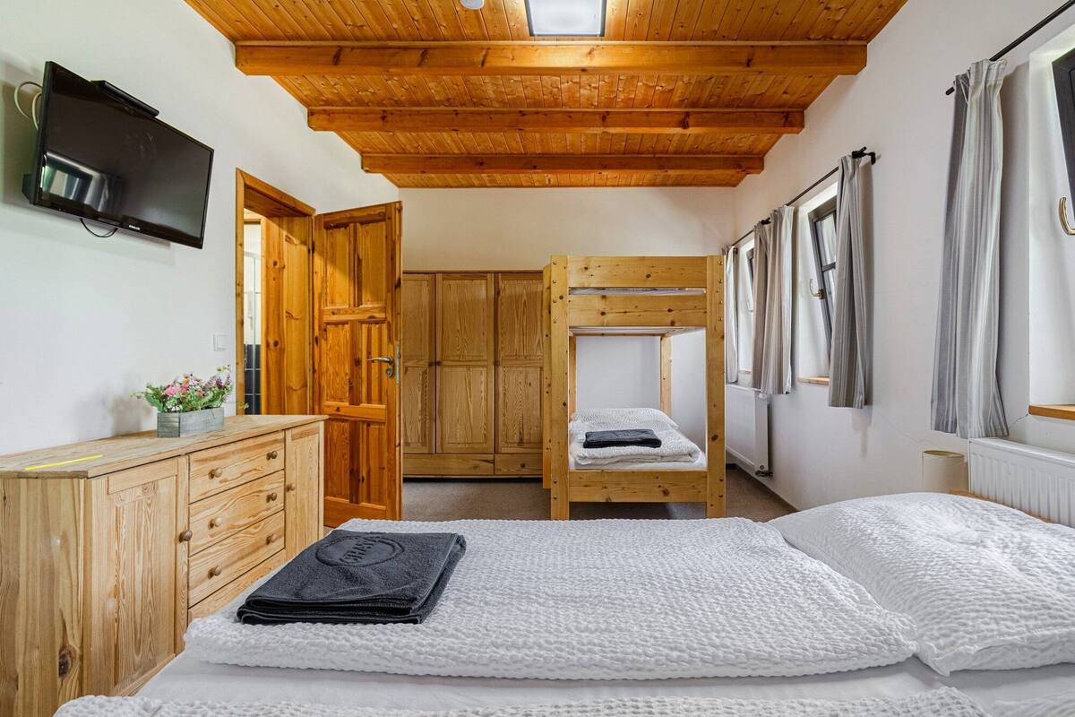 A bedroom with a bunk bed, wooden wardrobe, and a television on the wall.