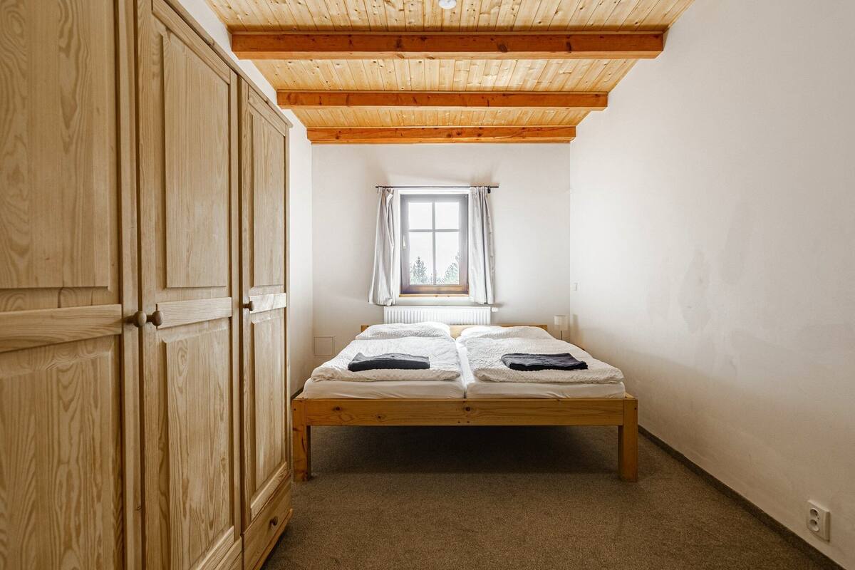 A small bedroom with a wooden bed, a window with curtains, and a wooden wardrobe.