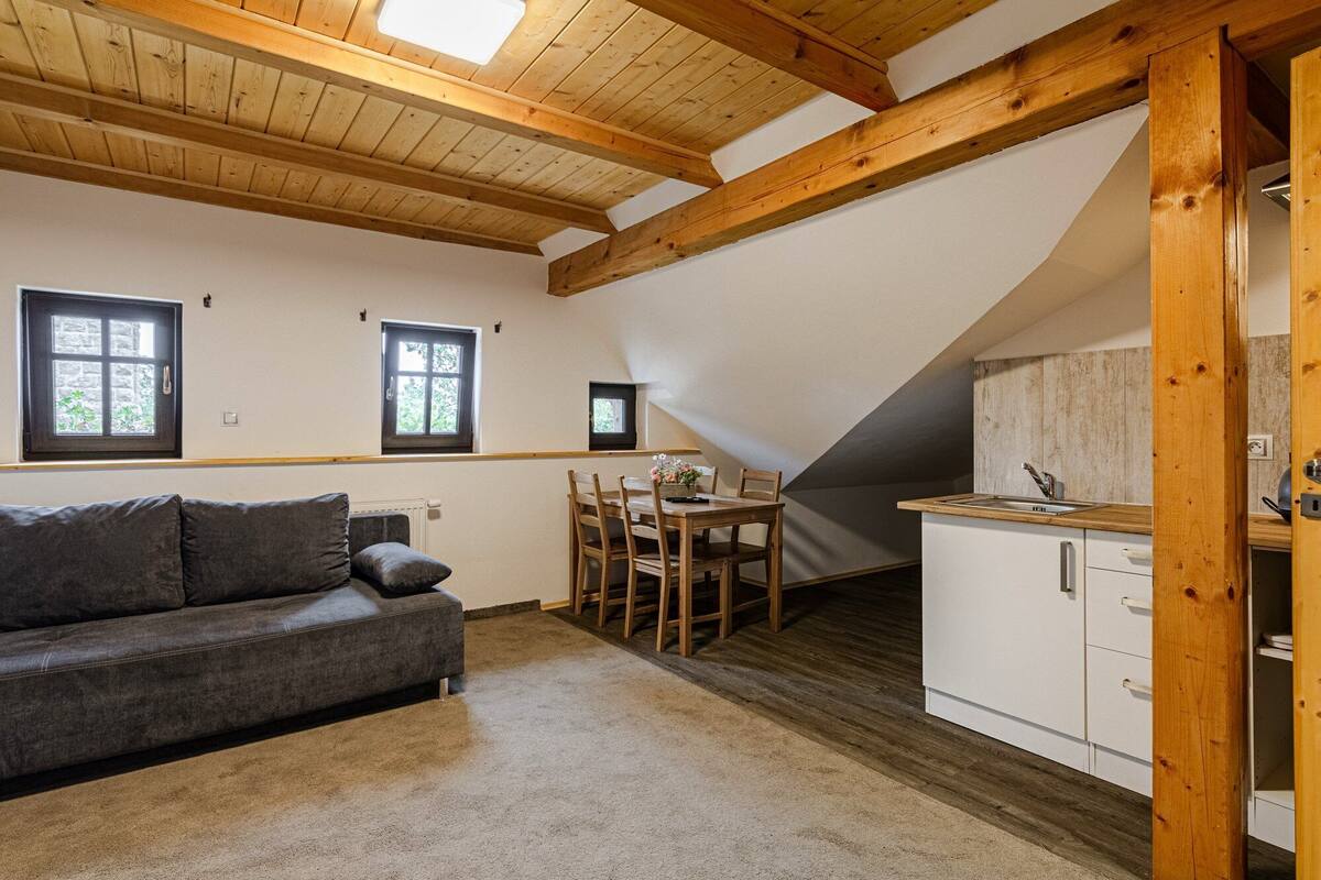 A cozy room with a wooden ceiling, a gray sofa, a dining table with chairs, and a kitchenette with a sink and cabinets.