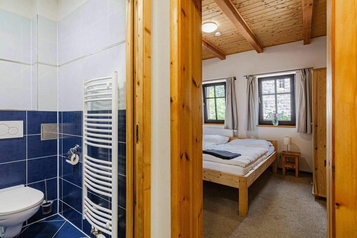 A bedroom with a wooden bed, a window with curtains, and a view of greenery outside.