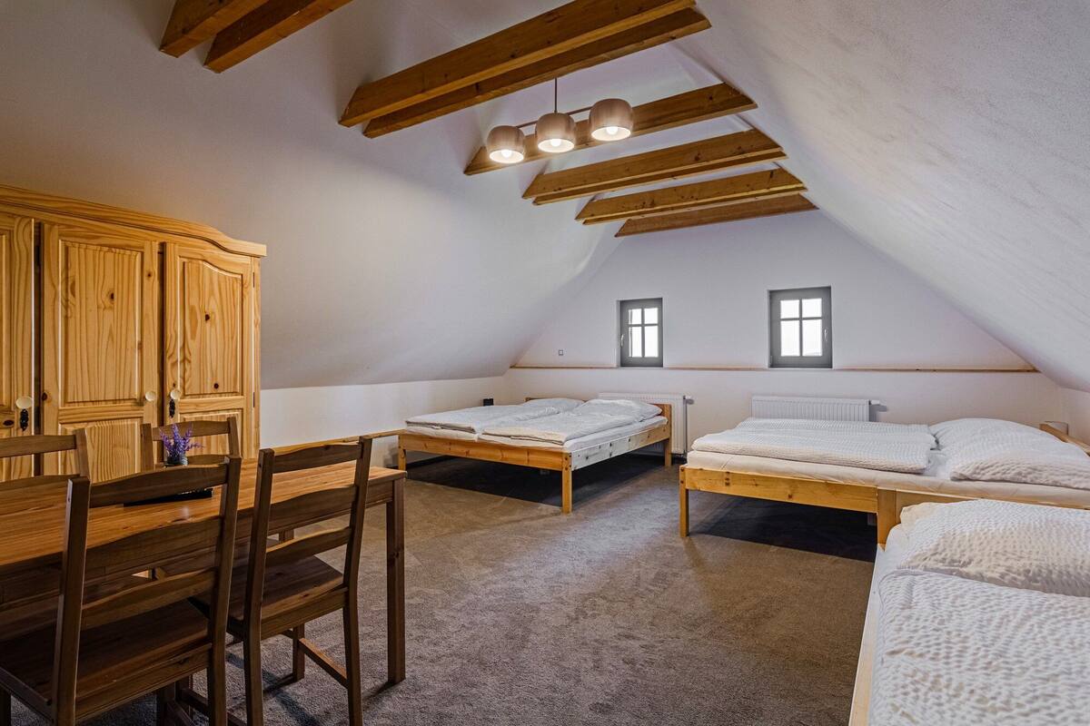 A cozy attic bedroom with two beds, a wooden wardrobe, and a dining table.