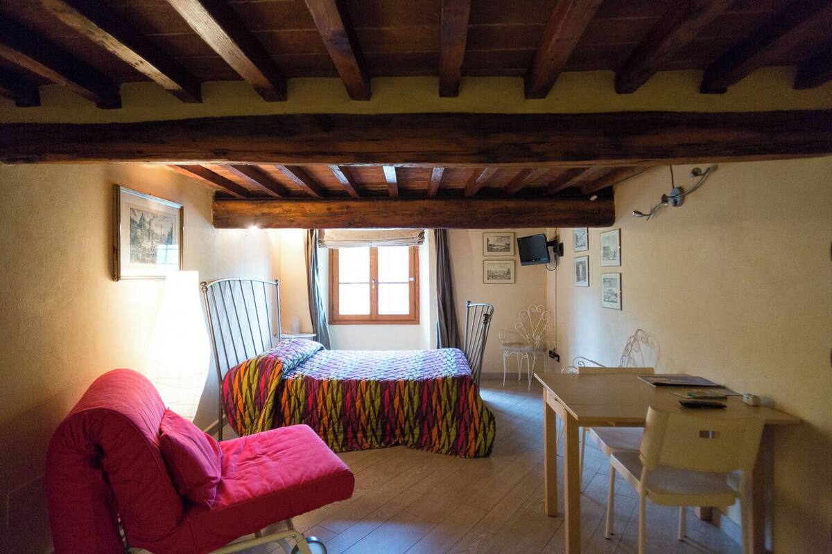 Una habitación pequeña y acogedora con cama, una silla roja, un escritorio y una ventana.