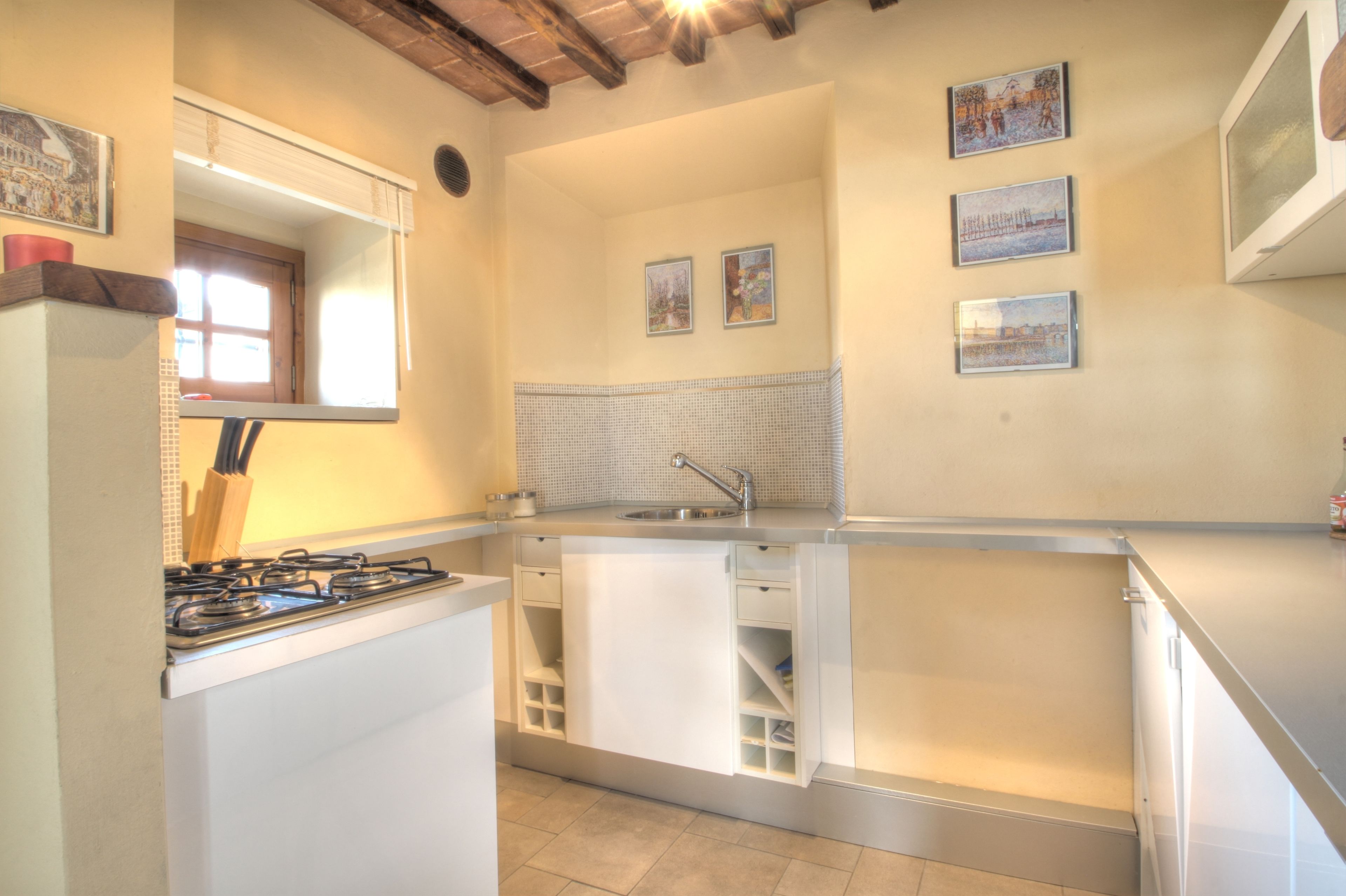 Cocina compacta con estufa a gas, un lavamanos y un ventanal. Hay tres cuadros en la pared.