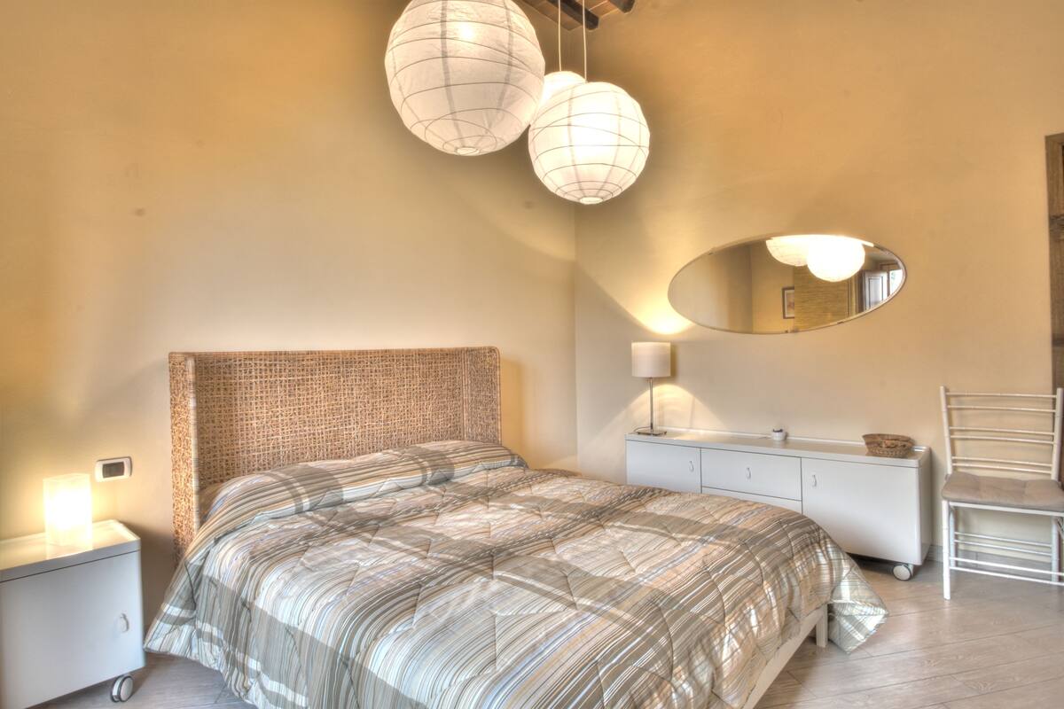 Un dormitorio con una cama grande, una mesita de noche, un aparador, una silla y dos lámparas colgantes.