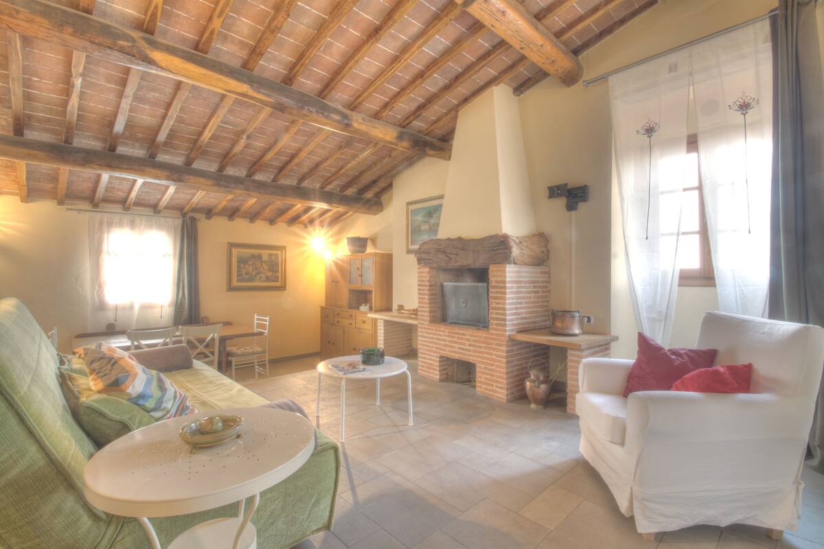 Una sala de estar acogedora con chimenea, un sofá, un sillón blanco y un comedor.