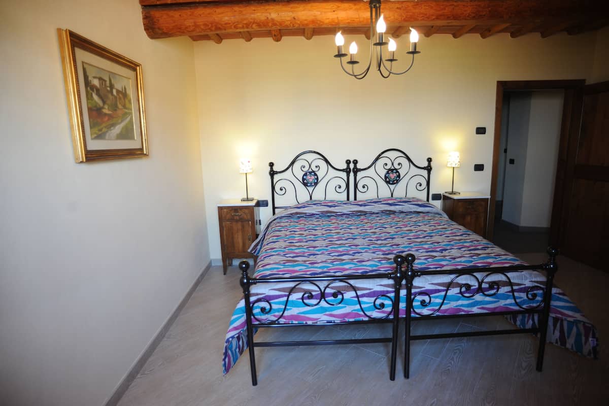 Un dormitorio con cama, cabecera de madera, candelabro, lámparas de noche y un cuadro enmarcado en la pared.