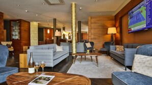 A modern hotel lobby with sofas, a coffee table, and a television displaying a tennis match. - Bacchus Hotel (Bensheim)