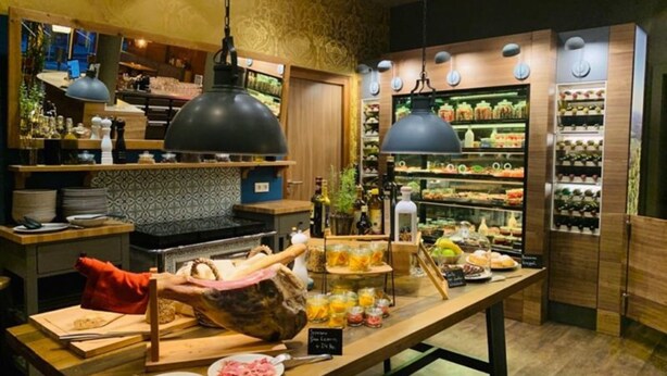 A restaurant with a wooden counter, hanging lights, and a variety of food items displayed. - Bacchus Hotel (Bensheim)