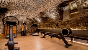A gym with stone walls and wooden flooring, equipped with cardio and strength training machines. - Bacchus Hotel (Bensheim)