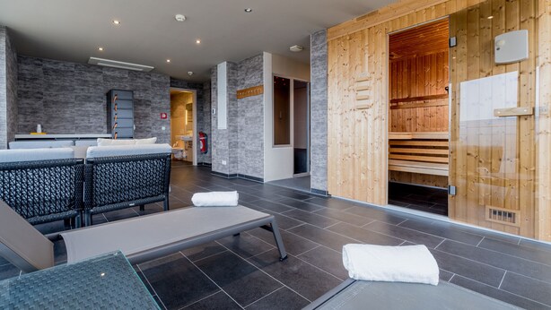A modern spa area with a massage table, seating area, and a sauna. - Bacchus Hotel (Bensheim)
