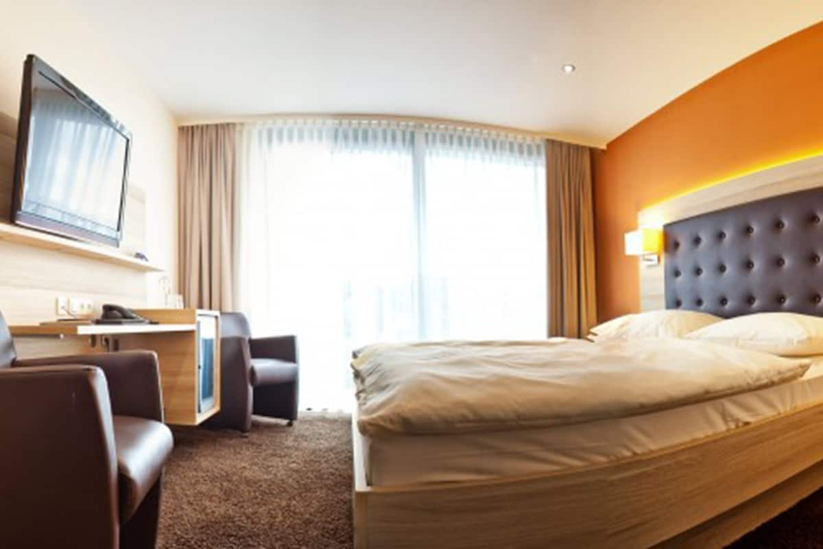 A hotel room with a bed, a desk with a computer, a chair, and a television.