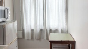 Una pequeña cocina americana equipada con microondas, refrigerador y una mesa de madera.