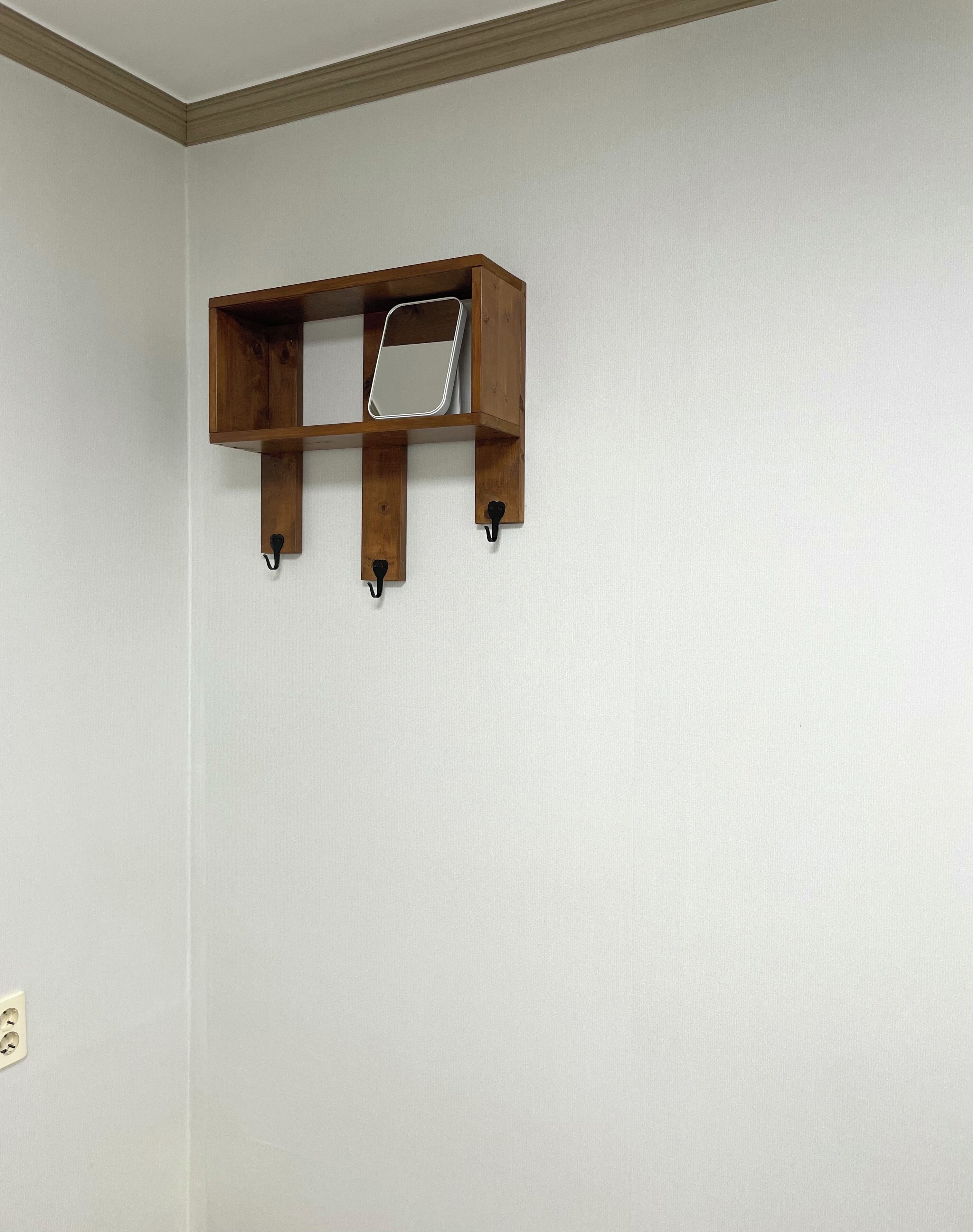 Une étagère en bois, dotée de crochets, fixée à un mur uni.