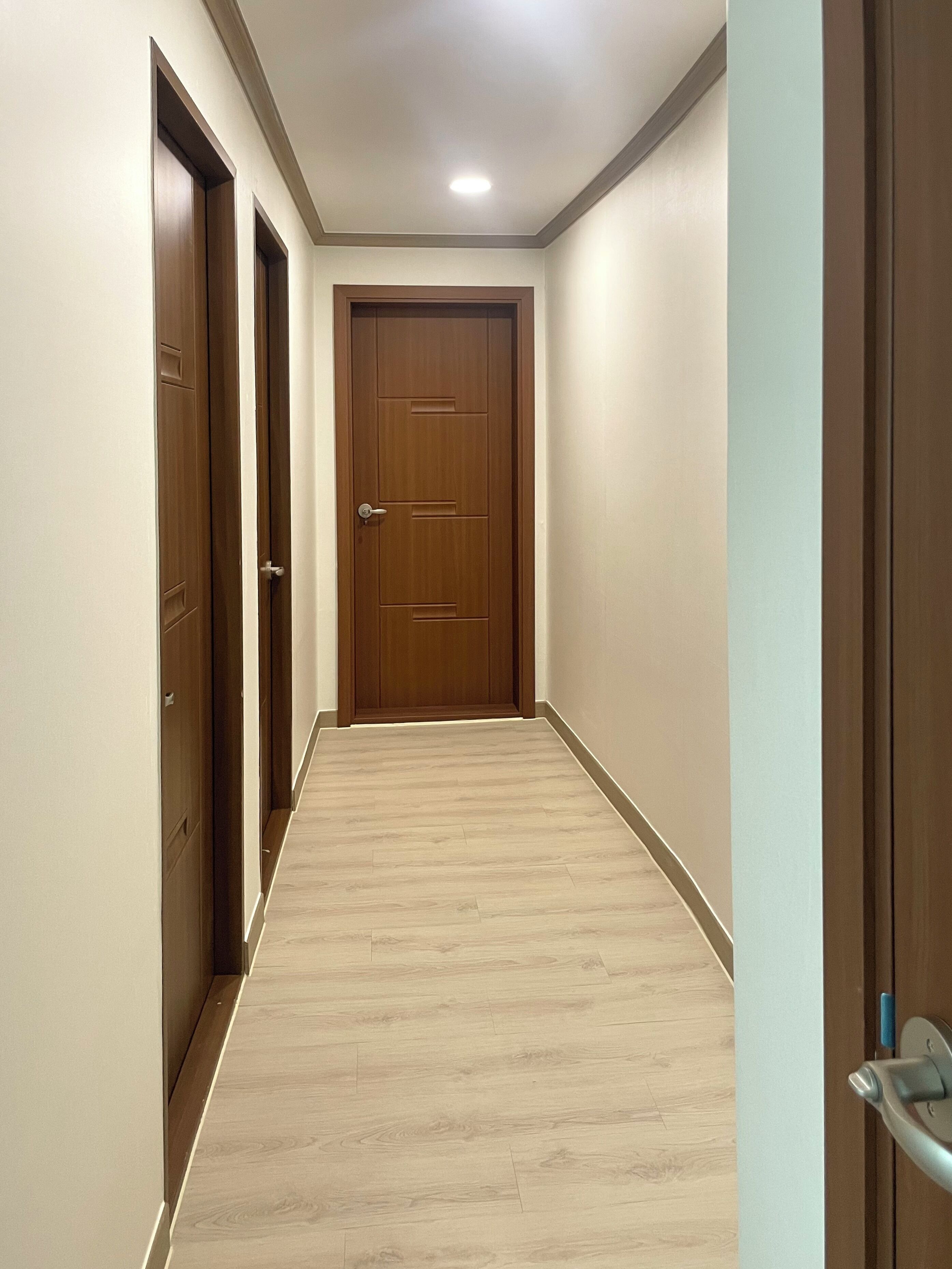 Un pasillo con tres puertas de madera, suelo de madera claro y una lámpara en el techo.