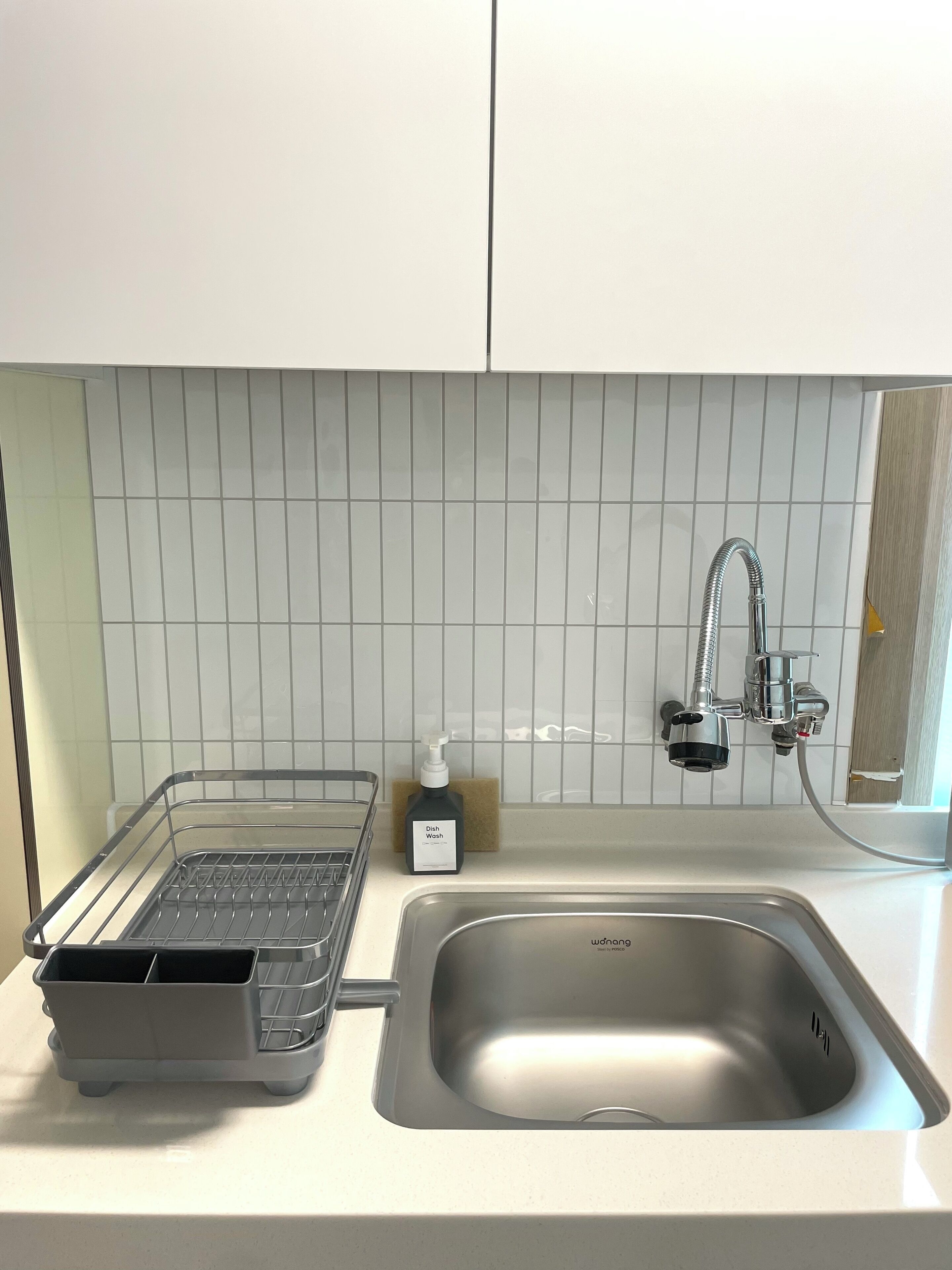 A kitchen with a stainless steel sink, a dish soap dispenser, and a drying rack.