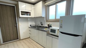 Una cocina con armarios blancos, un lavamanos de acero inoxidable, un microondas y un refrigerador blanco.
