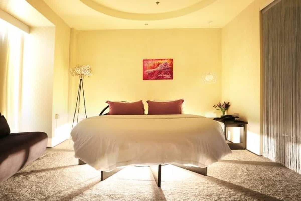 Un dormitorio con una cama grande, una mesita de noche, una lámpara de pie y un cuadro en la pared.