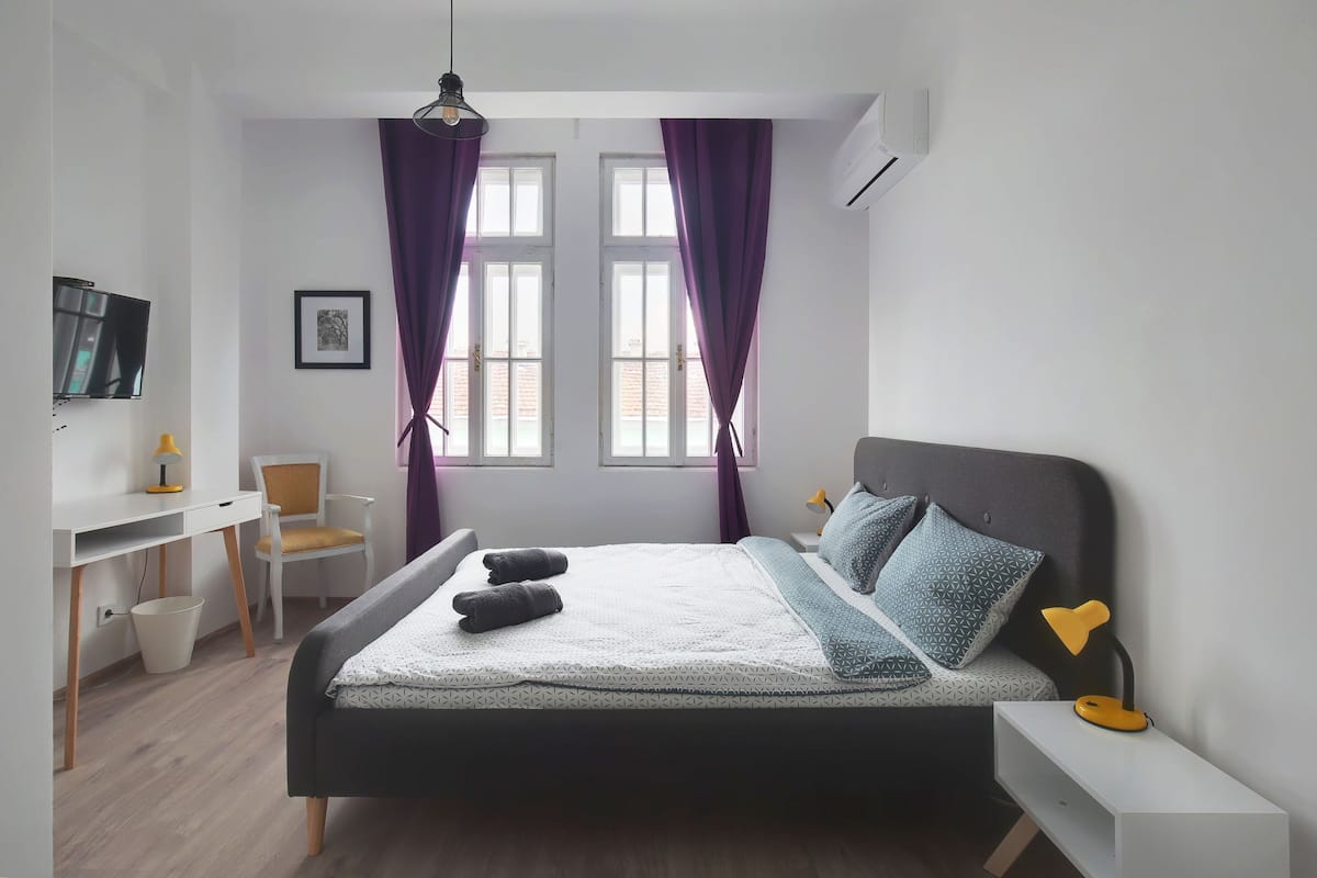 A modern bedroom with a bed, desk, chair, and a TV.