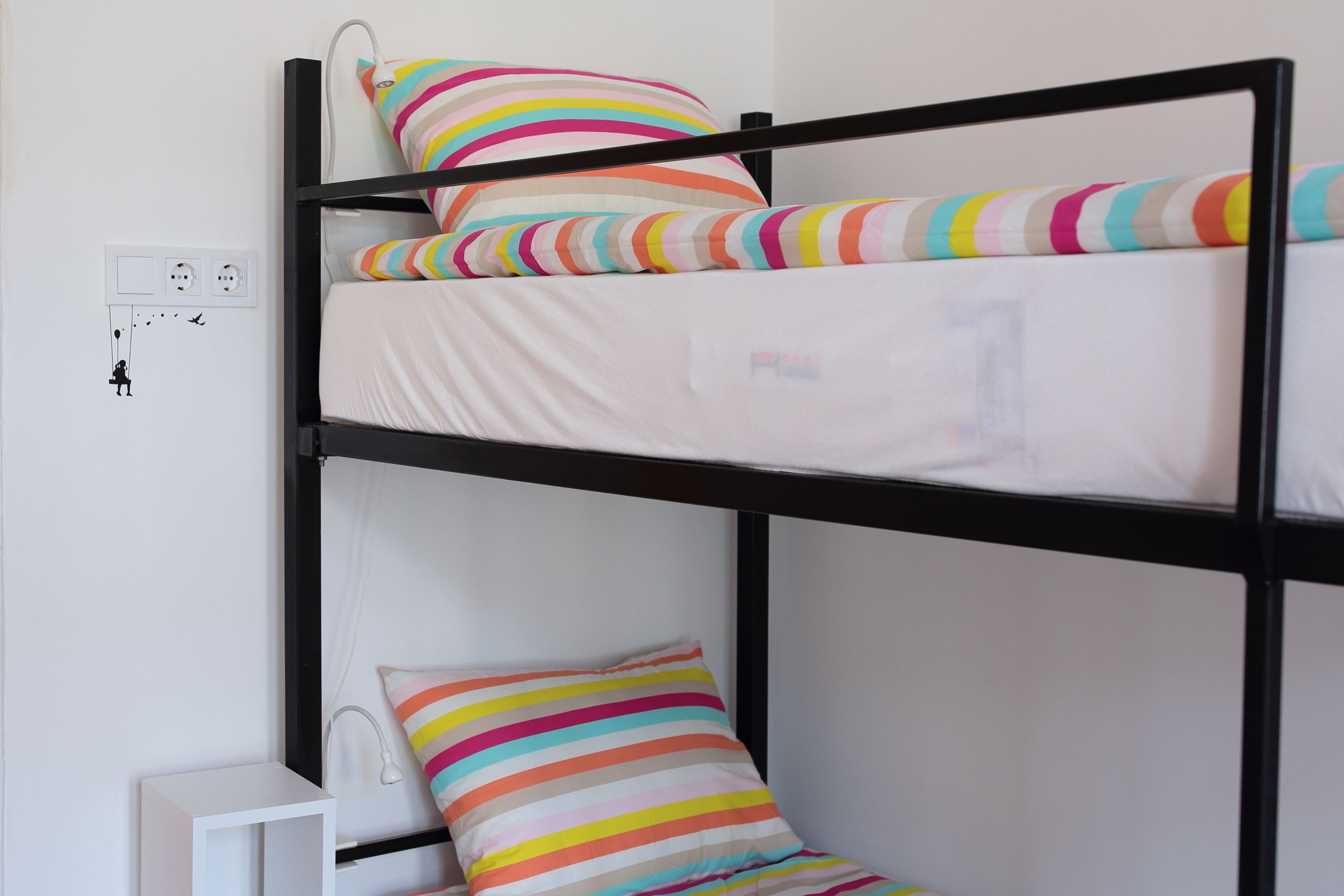 Una cama litera con almohadas a rayas y una mesita de noche con una lámpara.