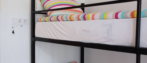 Una cama litera con almohadas a rayas y una mesita de noche con una lámpara.