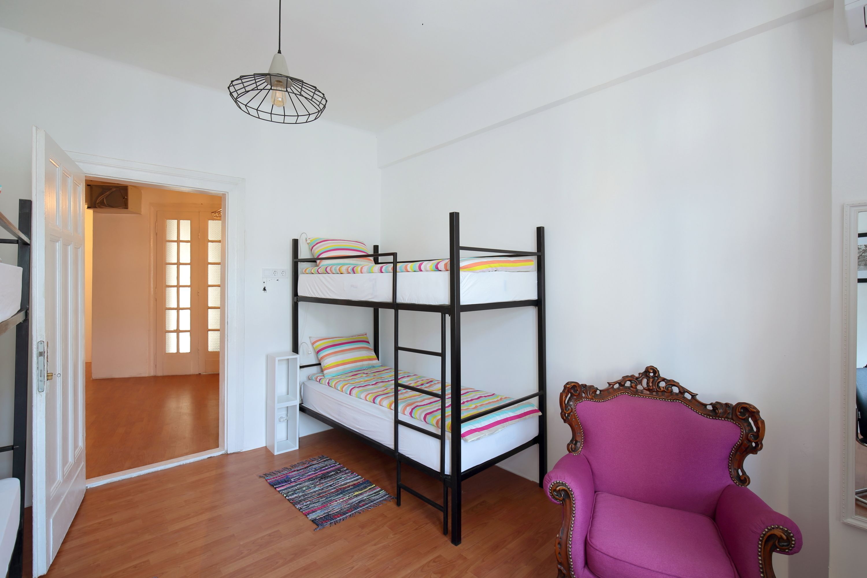 Habitació amb lliteres, terra de fusta, una cadira i un llum penjant.