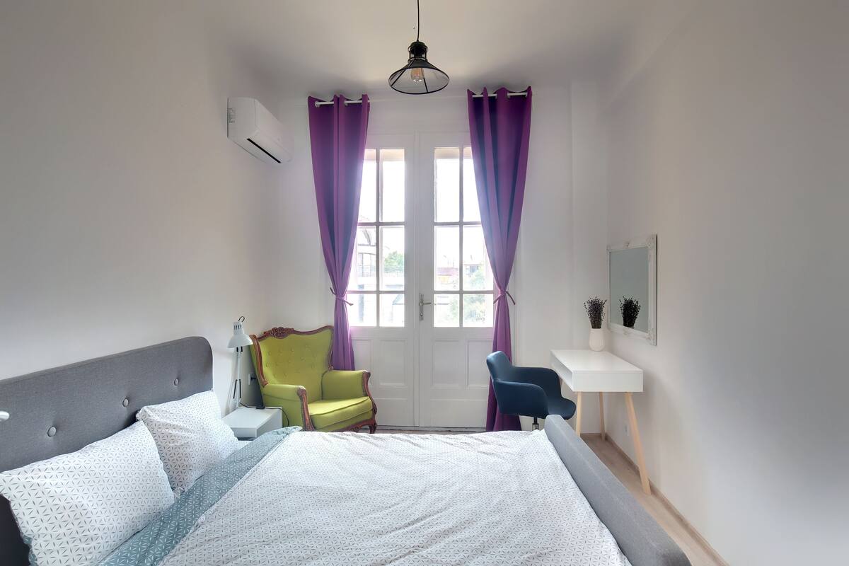 A bedroom with a bed, a desk, a chair, and a window with curtains.