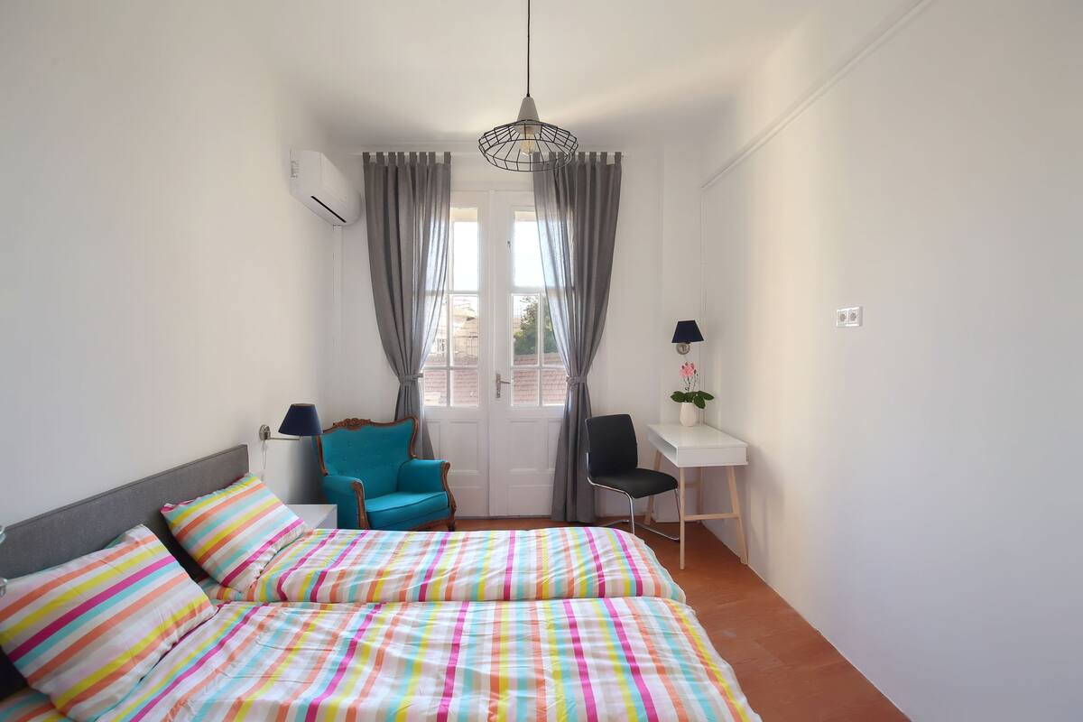 A bedroom with a bed, two chairs, a desk, and a window with curtains.