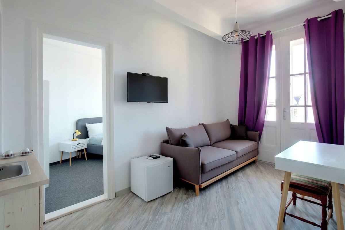 A modern living room with a grey sofa, a white table, and a TV mounted on the wall.