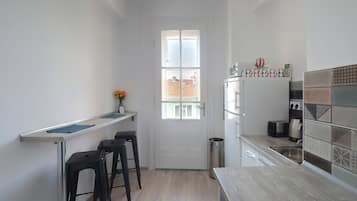 Cocina compacta con puerta blanca, una pequeña barra con taburetes, un lavamanos de acero inoxidable y un salpicadero azulejado.